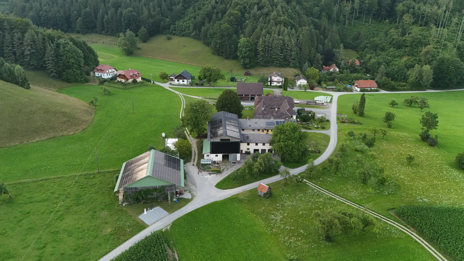 Luftaufnahme eines Bauernhofs im grünen Tal mit Photovoltaik am Wirtschaftsgebäude