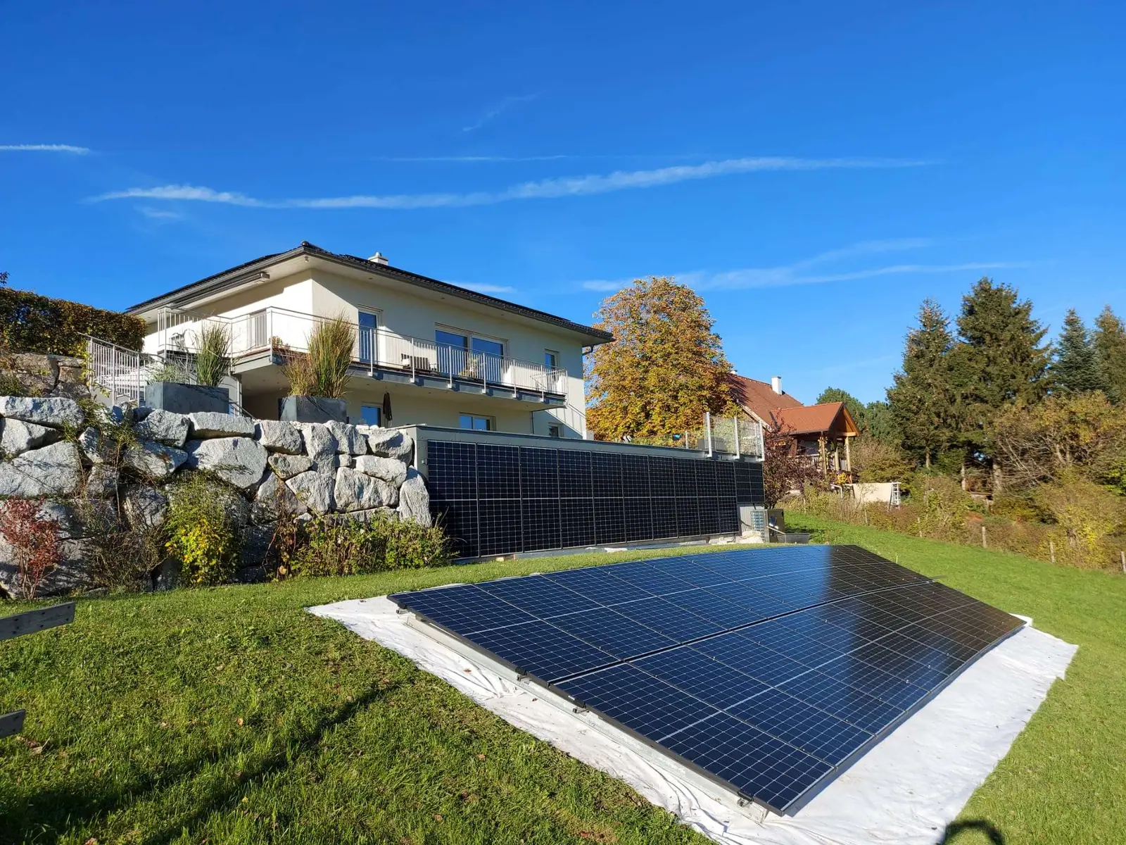 Einfamilienhaus mit Photovoltaik-Zaun an der Terrasse und Freiflächenmodulen im Garten