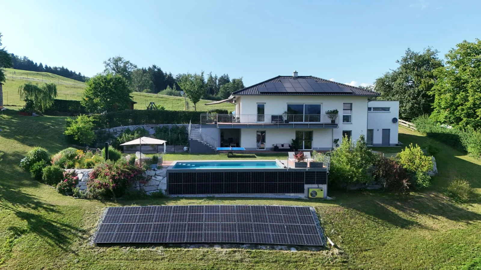 Modernes Einfamilienhaus mit Photovoltaik am Dach, am Pool-Zaun und als Freiflächenanlage im Garten